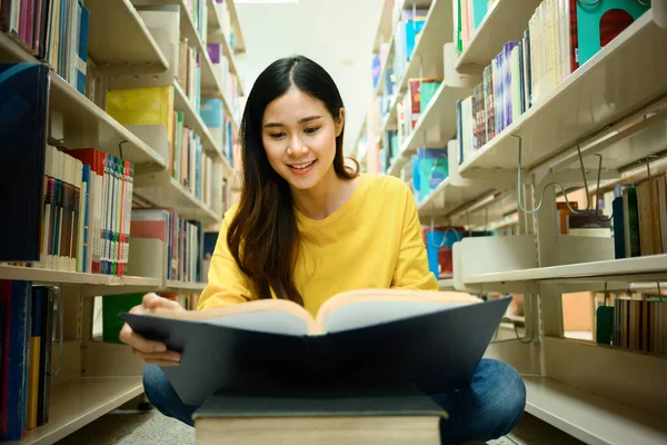 知識の概念 本棚の間の図書館に座って読書をする女子学生の笑顔 — ストック写真