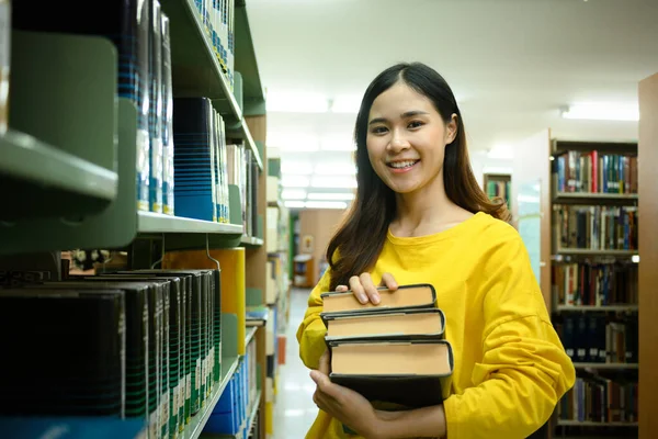 図書館の書棚の近くに立つ本を持つスマートな女性学生の肖像画 学習及び試験準備 — ストック写真