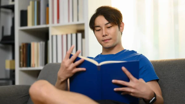 Tasasız Asyalı Adam Gündelik Kıyafetler Giyip Kanepeye Oturuyor Kitap Okuyor — Stok fotoğraf