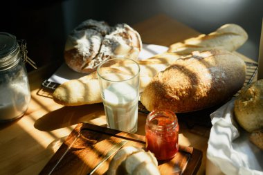 Mutfaktaki masanın üzerinde bir bardak süt ve fırınlanmış ekmek manzarası ve pencerenin güneş ışığı.. 