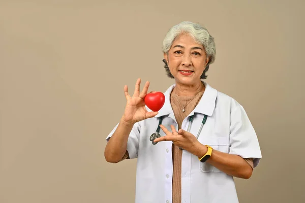 Positive Senior Woman Doctor Holding Red Heart Isolated Beige Background — Stock Photo, Image