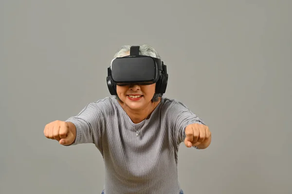 stock image Cheerful senior woman with virtual reality glasses simulating of driving car in VR glasses isolated on white background.