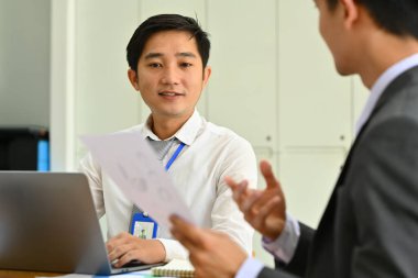 Asyalı erkek ofis çalışanı, iş arkadaşlarıyla proje istatistiklerini veya mali raporlarını tartışarak fikirleri paylaşıyor.