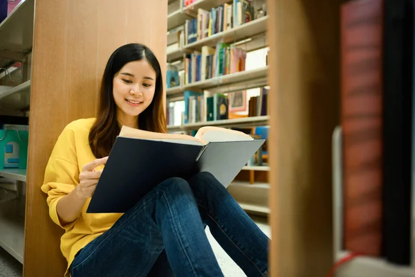 知識の概念 書棚の間の図書館の床に座って穏やかな女性学生 テキストブックを読む — ストック写真