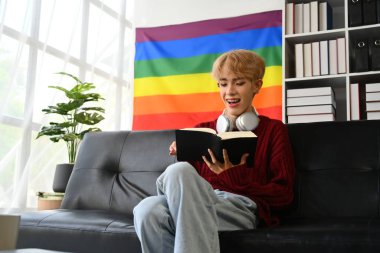 Rahat genç Asyalı eşcinsel adam koltukta en sevdiği romanı okuyor. LGBTQ, eğlence ve yaşam tarzı konsepti.