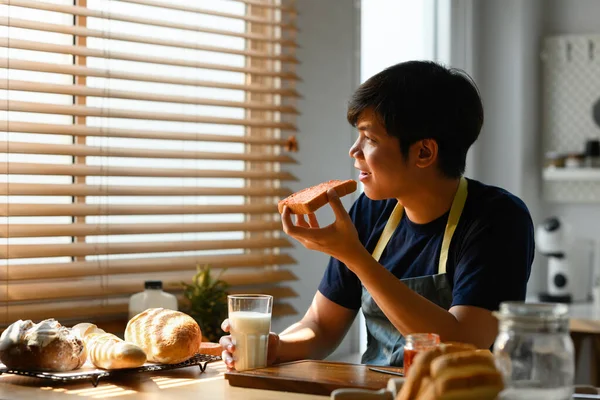 Безтурботний Молодий Азіатський Чоловік Їсть Свіжий Шматочок Хліба Сніданок Дивиться — стокове фото
