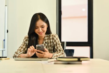 Akıllı telefon kullanan genç bayan ofis çalışanı, müşteriye uzaktan danışmak veya sosyal medyayı kontrol etmek.