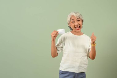 Heyecanlı, gri saçlı, kredi kartı tutan kadın pastel yeşil arka planda izole edilmiş..