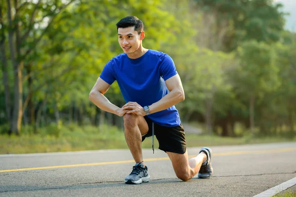 stock image Full length of handsome male athlete in fitness clothes stretching legs, warming up before sports training outdoors.