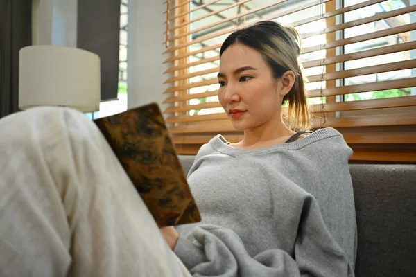 安详的千禧年女人穿着休闲装在家里沙发上看书 休闲和生活方式概念 — 图库照片