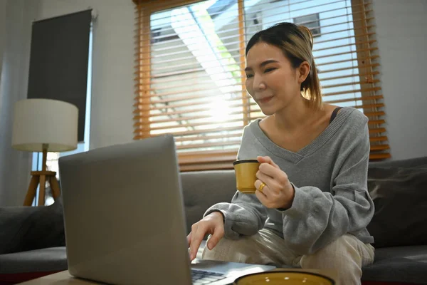 커피를 거실에서 노트북을 사용하는 아시아 여성을 가르치는 — 스톡 사진