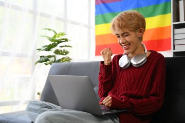 Heyecanlı genç Asyalı eşcinsel dizüstü bilgisayara bakıyor, kazanan evet hareketi yapıyor, başarıyı kutluyor..