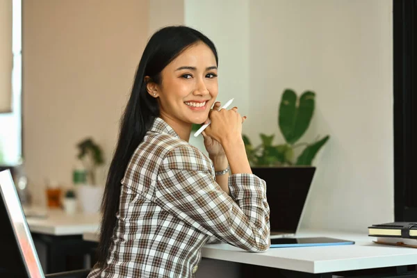 Portrait of young female secretary, office manager sitting in modern office and smiling to camera.
