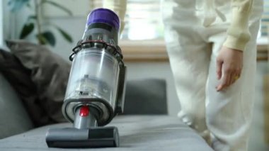 Modern elektrikli süpürgeyle oturma odasındaki kanepenin kirini temizleyemezsin. Ev, temizlik ve teknoloji konsepti.