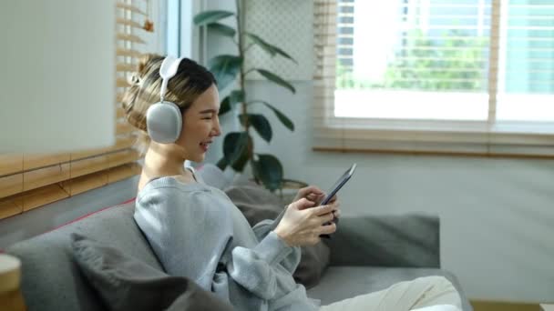 在家里带着耳机在数字平板电脑上玩电子游戏的快乐年轻女性的侧视图 — 图库视频影像