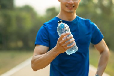 Sporcu elinde bir şişe su tutuyor, antrenmandan sonra dışarıda dinleniyor. Fitness, eğitim ve sağlıklı yaşam tarzı.