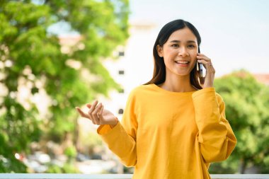Çekici genç Asyalı kadın ofis binasının balkonunda dururken cep telefonuyla arkadaşlarıyla konuşuyor..