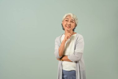 Gülümseyen, son sınıf öğrencisi, çenesine dokunan, düşünceli, mavi arka planda duran bir kadın..