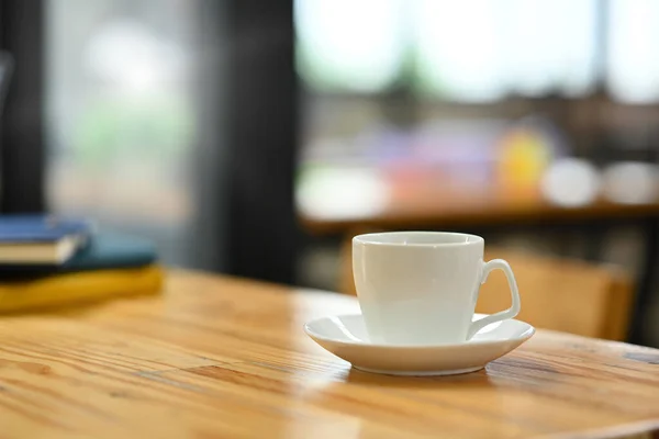 Closeup white cup of coffee and books on wooden office desk. Empty area left side of image for your text.