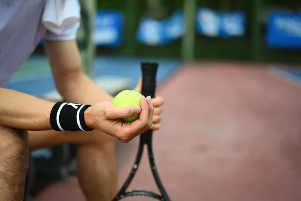 テニスコートのベンチに座ってボールラケットを保持する男性テニスプレーヤーの手に焦点を選択します — ストック写真