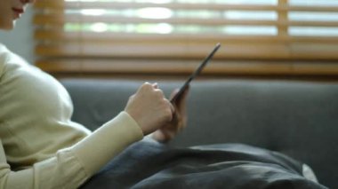 Mutlu genç bir kadın evdeki kanepede otururken dijital tablette komik sosyal medya videoları izlemekten zevk alıyor..