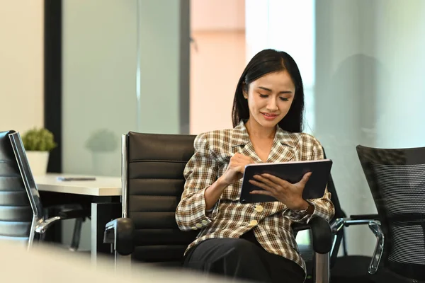 Modern young businesswoman sitting on office chair and using digital tablet. Business, people and technology.