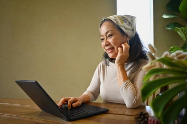 Güzel orta yaşlı bir kadın dizüstü bilgisayarında ailesiyle ya da arkadaşlarıyla görüntülü görüşme yapıyor. İnsanlar, teknoloji ve iletişim konsepti.