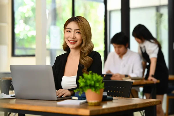 Portrait of young female secretary, office manager sitting in modern office and smiling to camera.