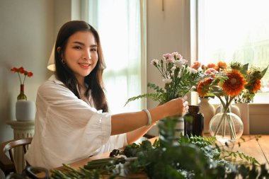 Çekici genç bayan farklı çiçeklerle güzel bir buket oluşturuyor, evde çiçek düzenlemekten zevk alıyor..