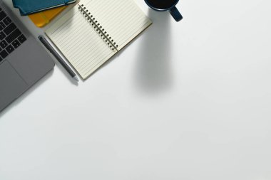 Boş not defteri, dizüstü bilgisayarı ve bir fincan kahvesi olan beyaz ofis masası. Kopyalama alanı olan üst görünüm.