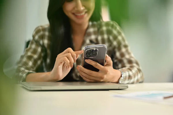 满意的年轻女性员工坐在办公桌前 用智能手机 发短信或社交媒体进行交流 — 图库照片