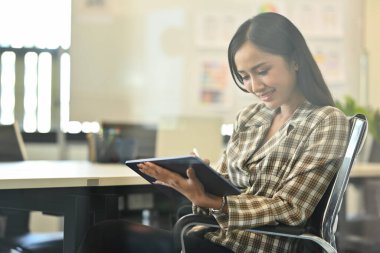 Dijital tablet kullanan, yaratıcı ofiste tasarım projesi üzerinde çalışan hoş bir bayan girişimci. Camdan bak.