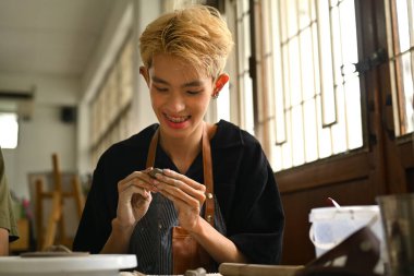 Gülen adam atölyede çömlekçilik yapmaya başlamadan önce kil yoğuruyor. Sanat terapisi, ev içi yaşam tarzı aktiviteleri ve hobiler konsepti..
