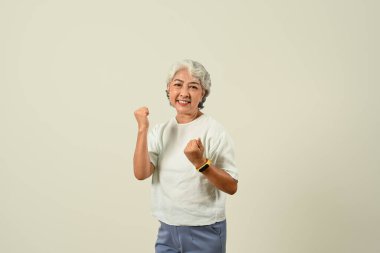 Neşeli yaşlı kadın elini kaldırıyor, bej arka planda izole edilmiş zafer işareti yapıyor..