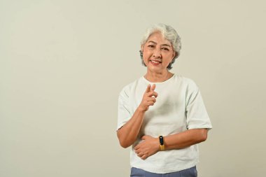 Gri arka planda izole edilmiş 60 'lı yaşlardaki beyaz saçlı kadın kamerayı doğal bir yüze ve kendine güvenen bir gülümsemeye çeviriyor..