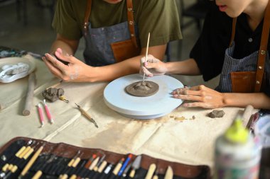 Bir adamın çömlek çarkında kil tabağı yontup sanat sınıfında el yapımı seramik yaparken kesilen görüntüsü..