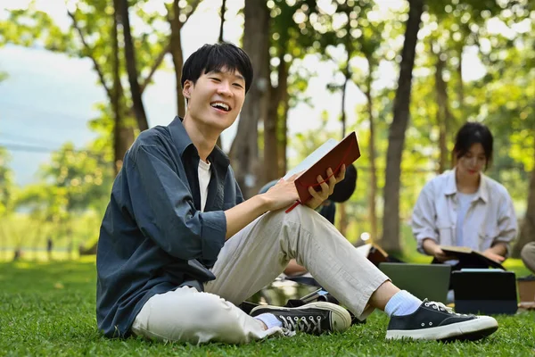 Uśmiechnięty Azjatycki Student Siedzący Trawie Czytający Książkę Styl Życia Edukacja — Zdjęcie stockowe