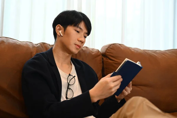 Όμορφος Άντρας Ασύρματα Ακουστικά Που Διαβάζει Βιβλίο Ελέγχει Πρόγραμμα Εργασίας — Φωτογραφία Αρχείου