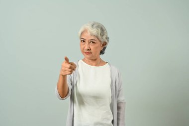 Katı, olgun bir kadının mavi arka planda izole edilmiş kamerayı işaret etmesi..