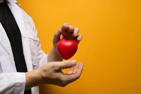 黄色の背景に赤いハートを持つ医師の手心臓学 寄付と医療の概念 — ストック写真