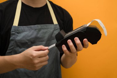 Elinde kredi kartı ve kablosuz banka ödeme terminali olan önlüklü bir adam. Elektronik para, temassız ödeme konsepti.