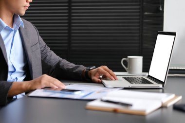 İş adamlarının mali belgelerle çalışmalarının ve iş yerinde dizüstü bilgisayar kullanmalarının yan görünümü.