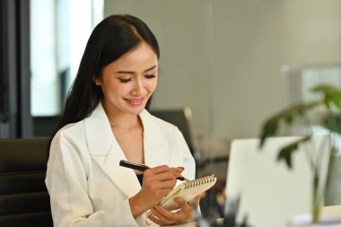 Çekici Asyalı girişimci kadın kişisel günlük planlamacıda not yazıyor ya da iş günü planlıyor.