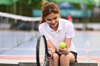 Elinde raketle tenis kortunda oturan genç ve güzel bir bayan..