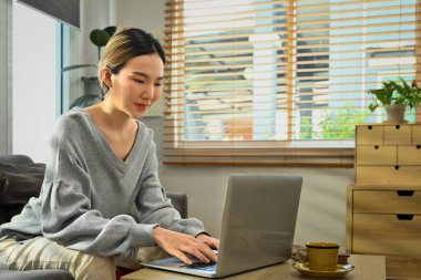 Evde dizüstü bilgisayar kullanan, sosyal ağda arkadaşlarıyla sohbet eden, film izleyen ve internetten alışveriş yapan mutlu genç bir kadın..