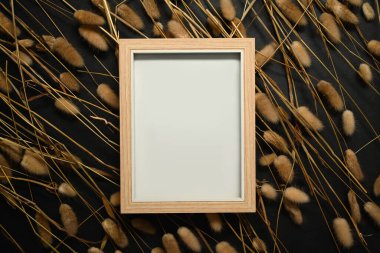 Ahşap çerçeve kurumuş tüylü tavşan kuyruğu ile çevrili siyah arka planda çimenler.