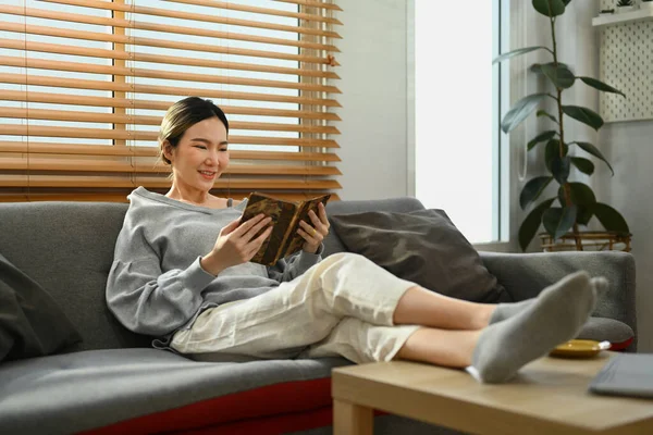 松驰的亚洲女人坐在舒适的沙发上看书 休闲和生活方式概念 — 图库照片