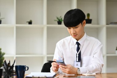 Yakışıklı bir ofis çalışanı akıllı telefondan mesajları ya da e-postaları kontrol ediyor. İnsanlar, teknoloji ve iletişim.