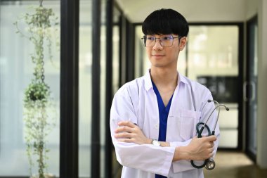 Pencerenin yanında duran steteskoplu beyaz önlüklü, gülümseyen pratisyen..