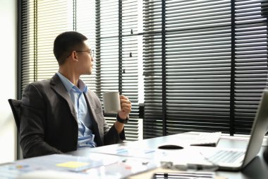 Ofis masasında oturan düşünceli bir işadamı, başka yere bakıyor, kariyer vizyonunu düşünüyor..